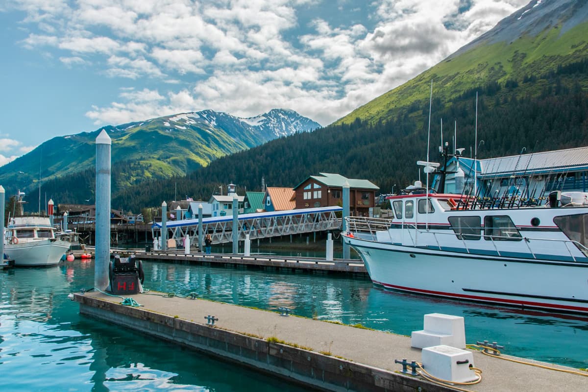 Boats parked in Seward Harbor with colorful buildings and mountains in the background in Seward, Alaska