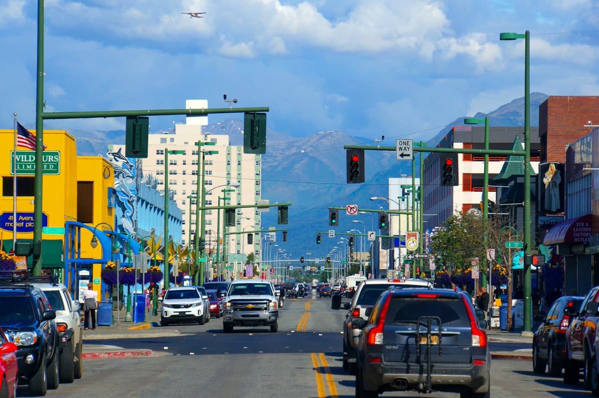 Cars driving down a busy, colorful street with mountains in the background in Anchorage, Alaska