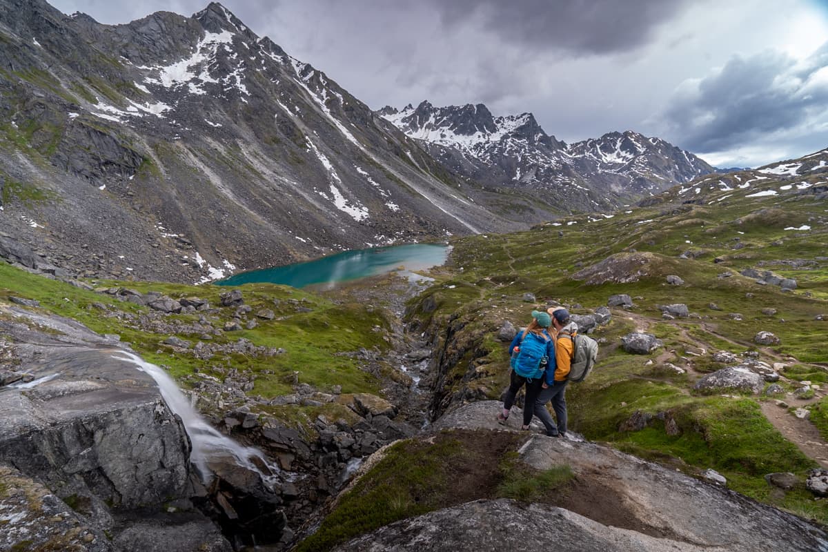Couple standing on a rocky outcropping, overlooking the Reed Lake and the Talkeetna Mountains along the Reed Lakes Trail in Hatcher Pass, Alaska