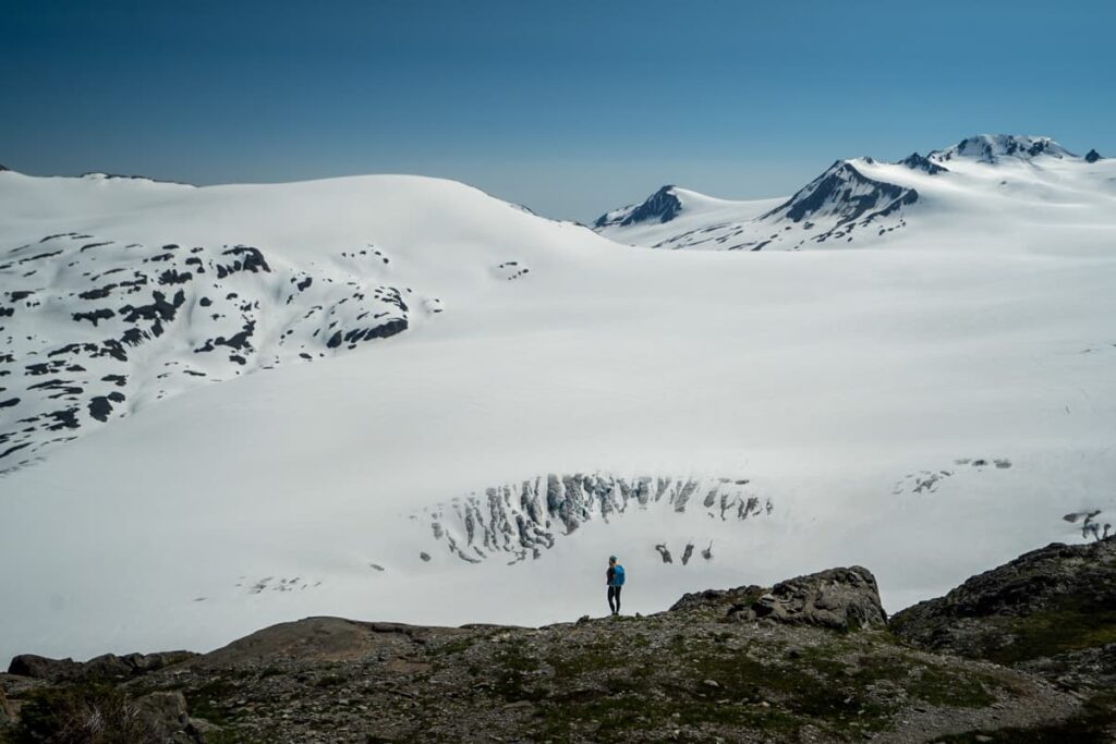 Woman standing on a ridgeline with the Harding Icefield in the background with Kenai Fjords National Park in Seward, Alaska