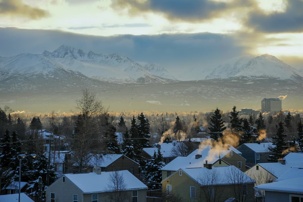 Houses with steam coming out of chimneys with snowy mountains in the background in Anchorage, Alaska