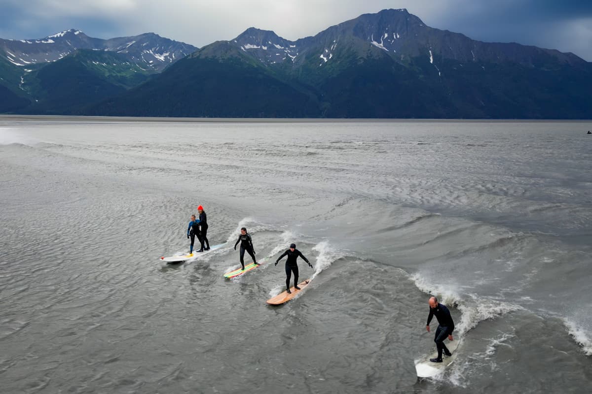 Surfers riding a boretide in the Turnagain Arm with Kenai Mountains in the background near Anchorage, Alaska