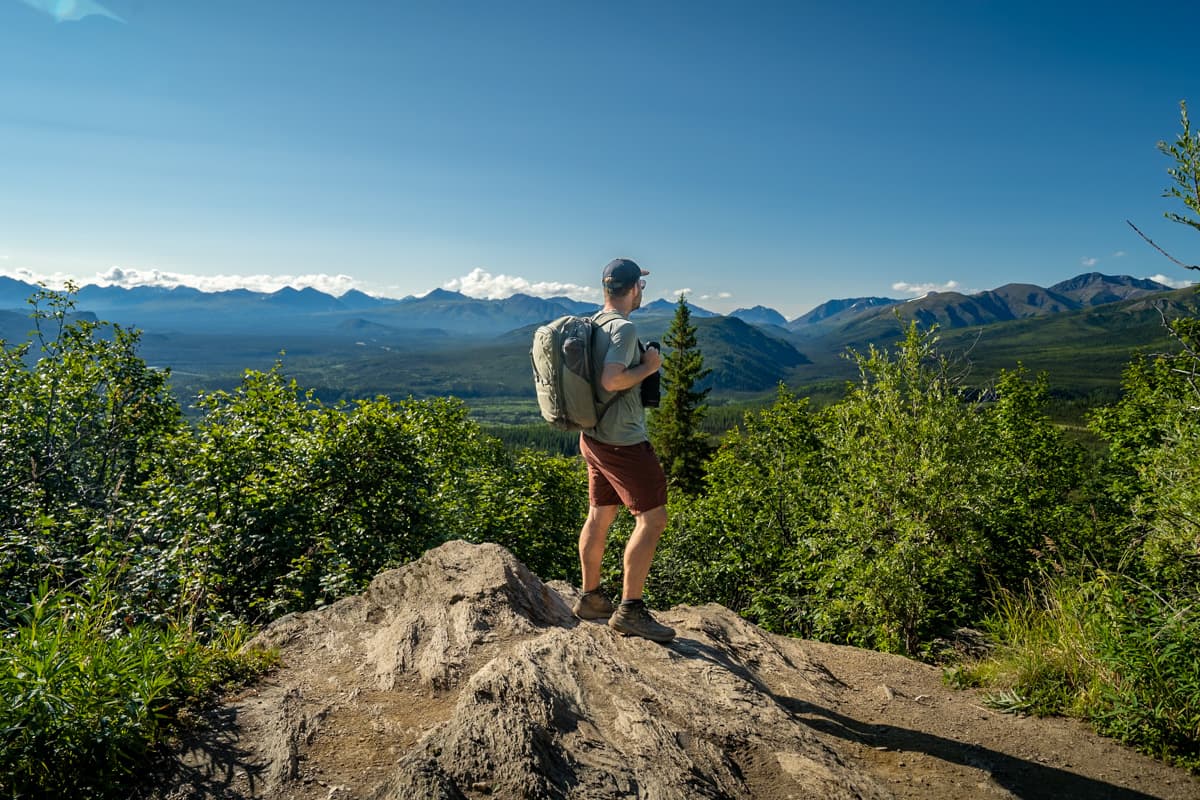 Man standing on a rocky outcropping with the Alaska Mountain range in the background along the Mount Healy Overlook Trail in Denali National Park in Alaska