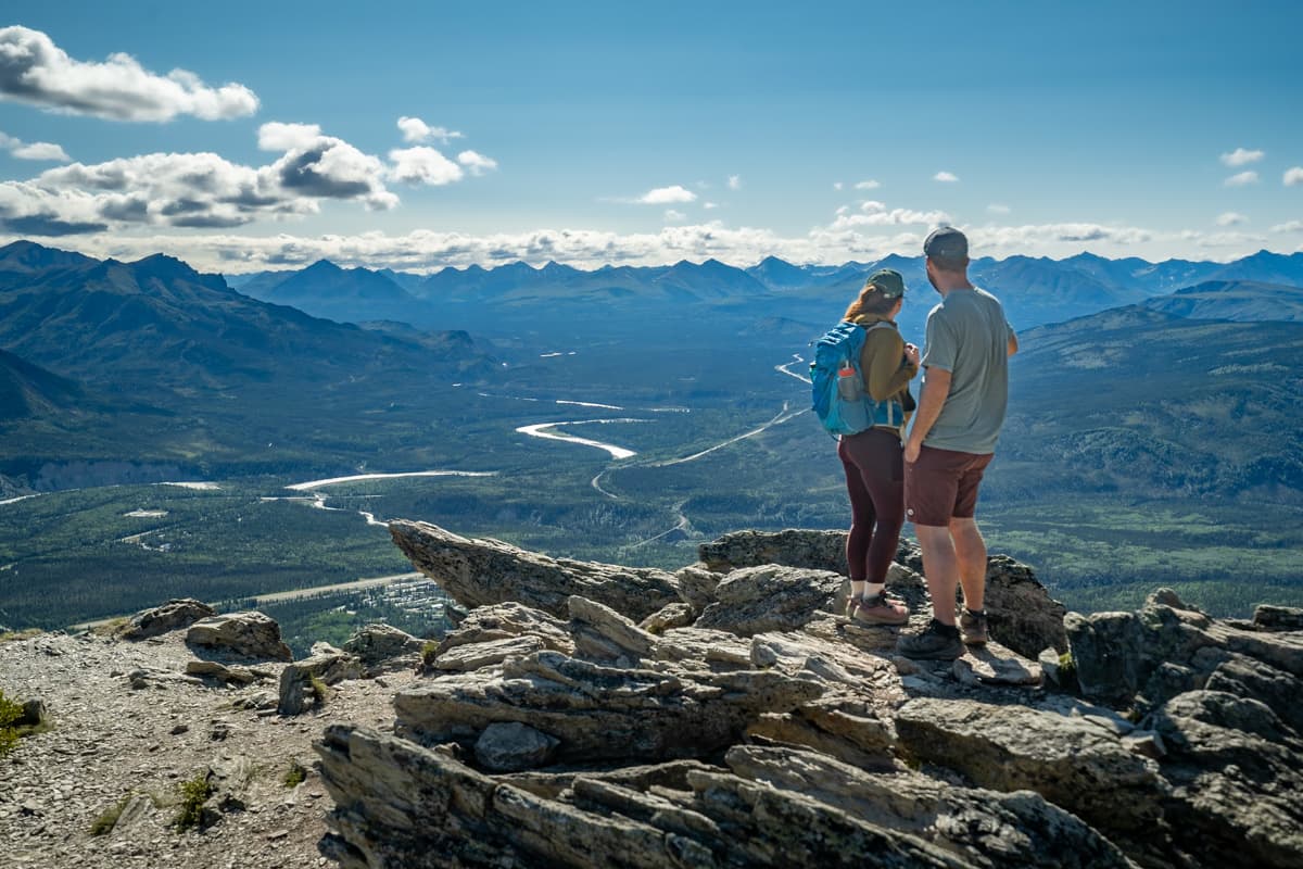 Couple standing on a rocky outcropping along the Mount Healy Overlook Trail with the Alaska Mountain range with the Nenana River valley in the background in Denali National Park in Alaska