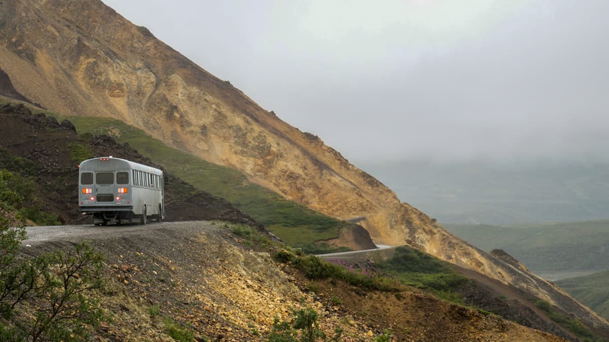 Shuttle driving on a Denali Park Road curving around the mountains in Denali National Park in Alaska