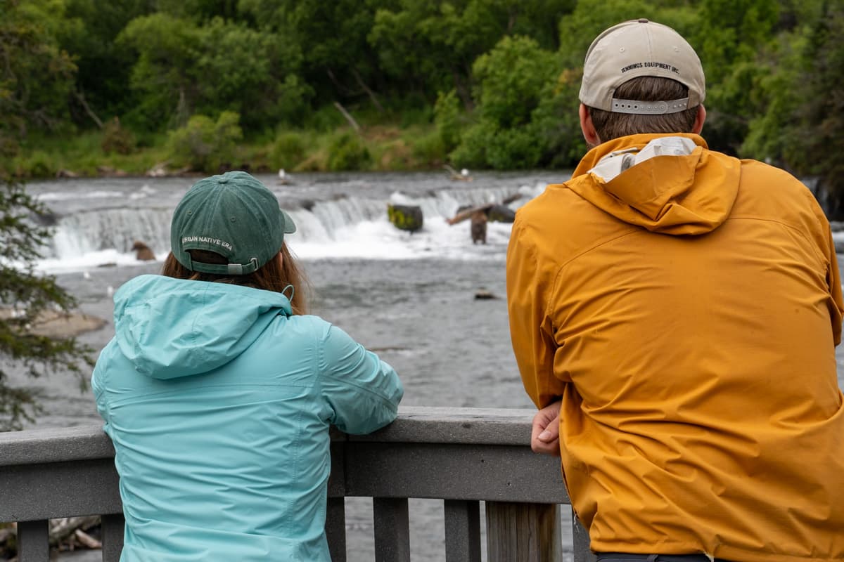 Couple sitting on a wooden observation platform overlooking brown bears in Brooks Falls in Katmai National Park in Alaska