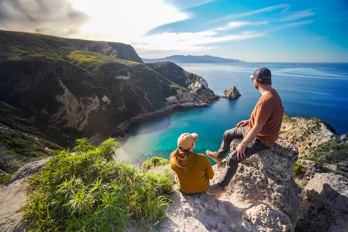 Couple sitting on a rocky outcropping overlooking cliffsides and sea stacks in Potato Harbor on Santa Cruz island in Channel Islands National Park, California