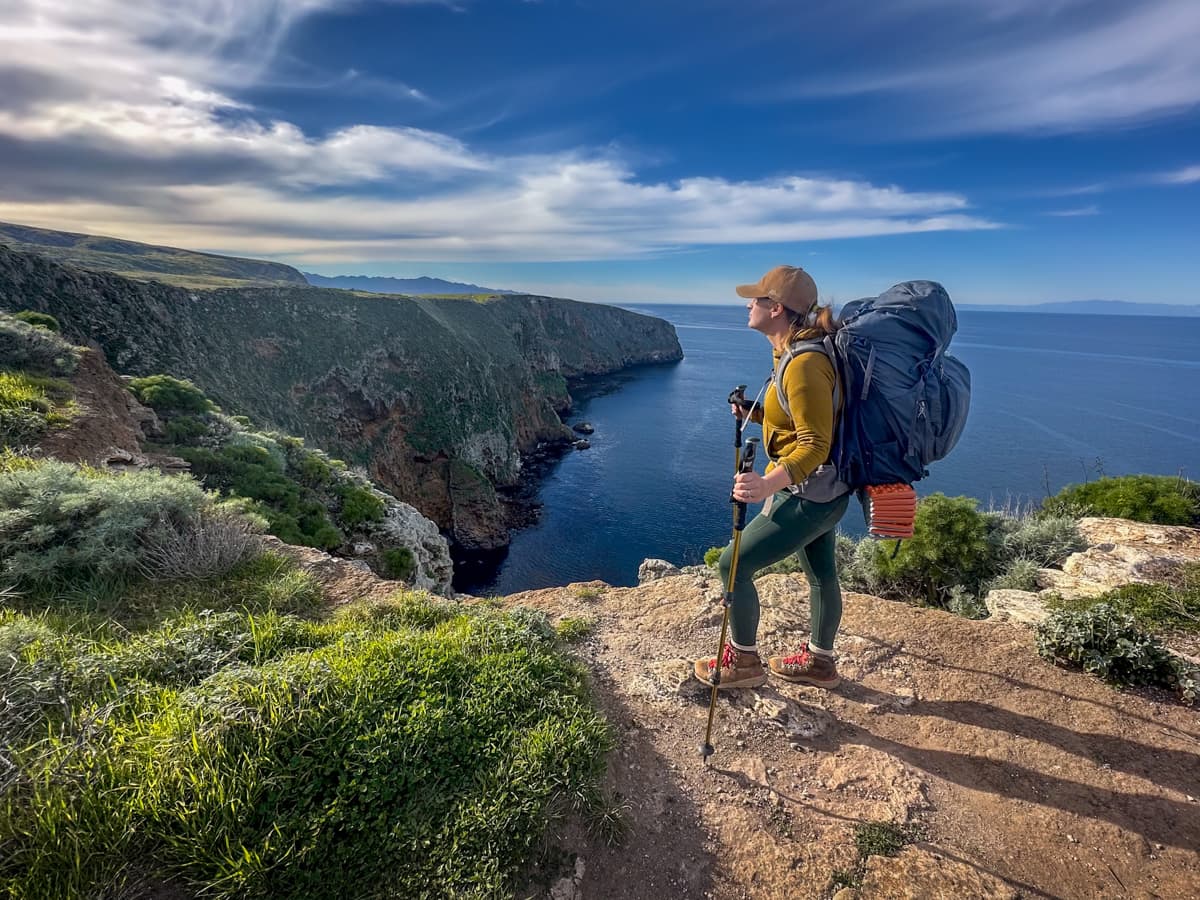 Woman wearing a backpack with the cliffside of Santa Cruz island in the background in Channel Islands National Park, California
