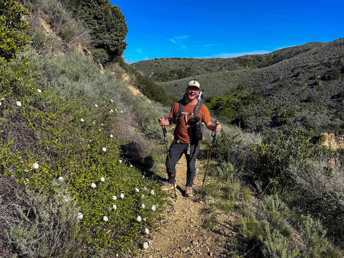Man smiling next to a hill of wildflowers along the Del Norte Trail on Santa Cruz Island in the Channel Islands National Park, California