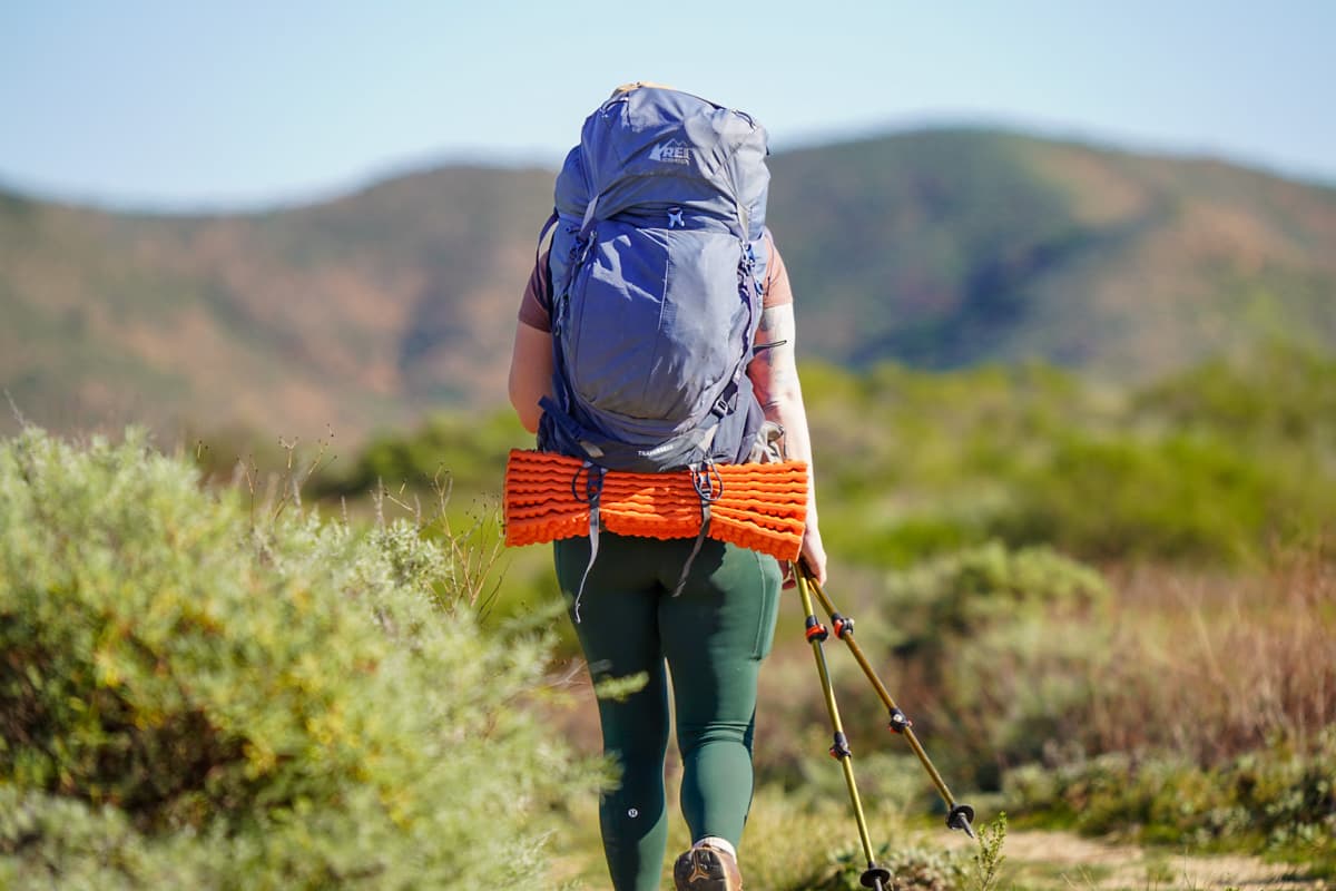 Woman walking with a backpack with greenery and hills in the background on Santa Cruz island in the Channel Islands National Park, California