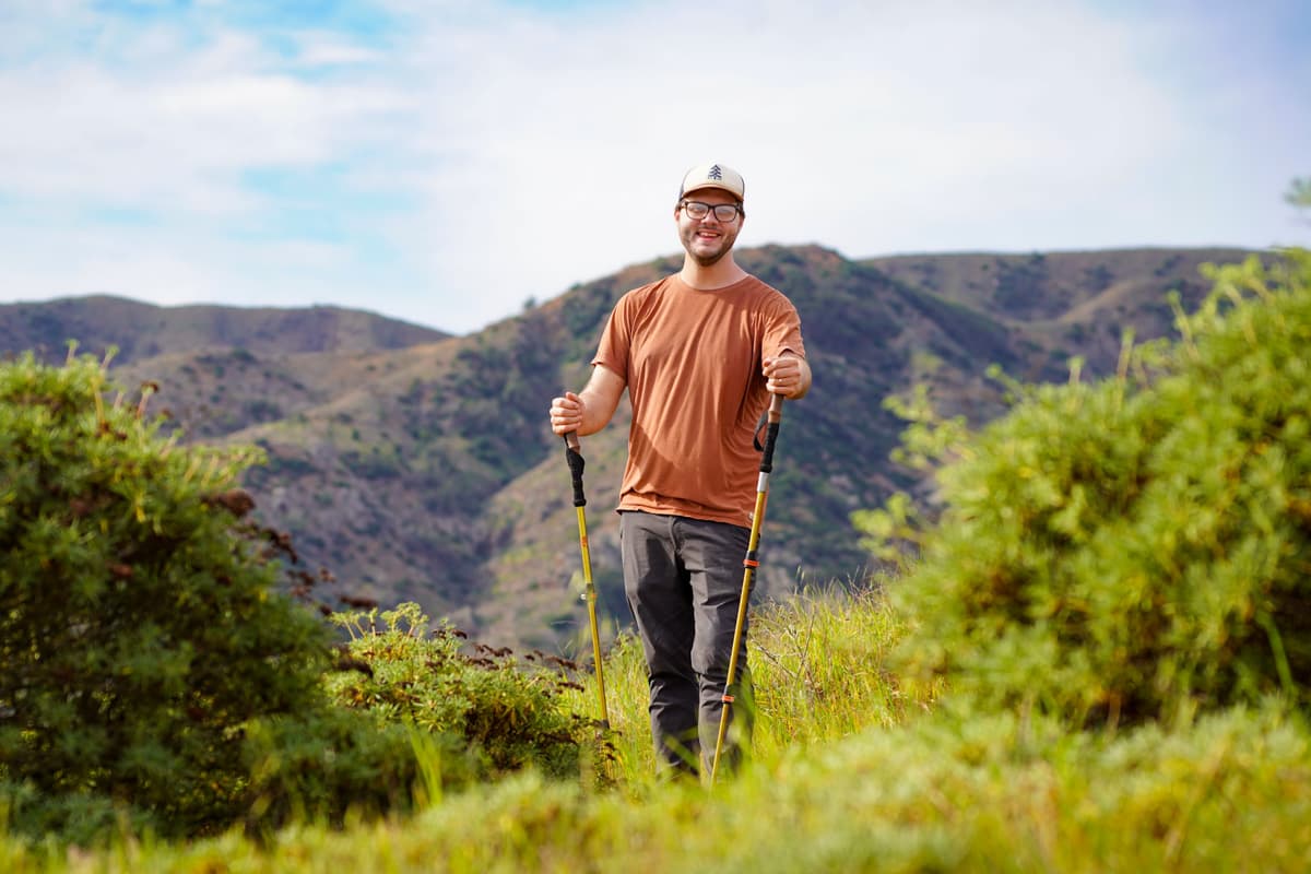 Man with trekking poles smiling in front of rolling green hills on Santa Cruz Island in the Channel Islands National Park, California