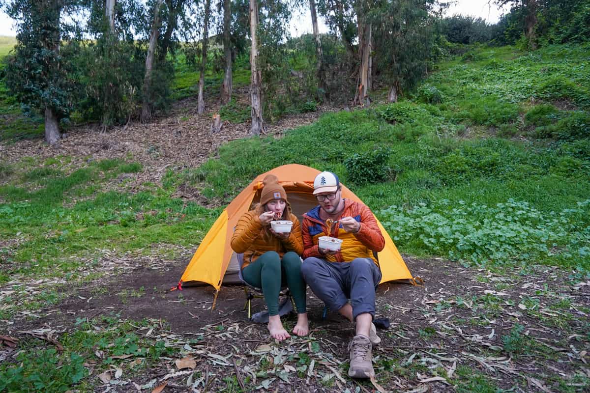Couple eating bowls of noodles in front of their tent in Scorpion Campground on Santa Cruz island in Channel Islands National Park