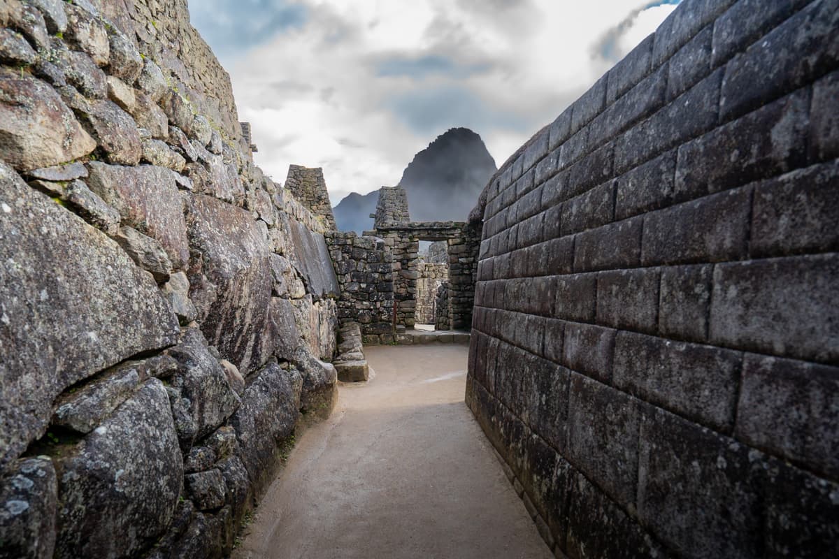 Stone walls and doorway with low-hanging clouds and Huayna Picchu mountain in the background at Machu Picchu, Peru