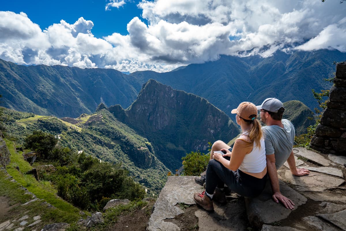 Couple sitting on the steps at the Sungate overlooking the city of Machu Picchu and Huayna Picchu Mountain in the background in Peru
