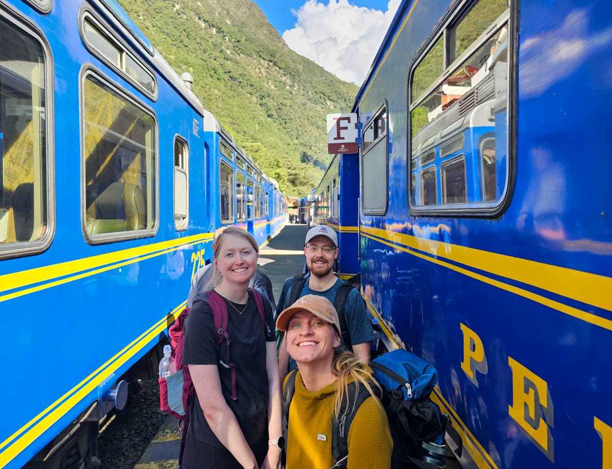 Three friends smiling in between train cars in Aguas Calientes, Peru
