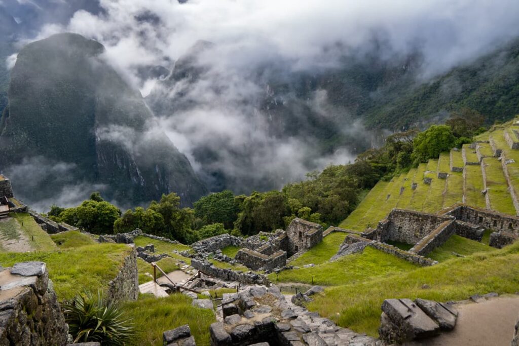 Agricultural terraces and building ruins with mountains and low-hanging clouds in the background in Machu Picchu, Peru
