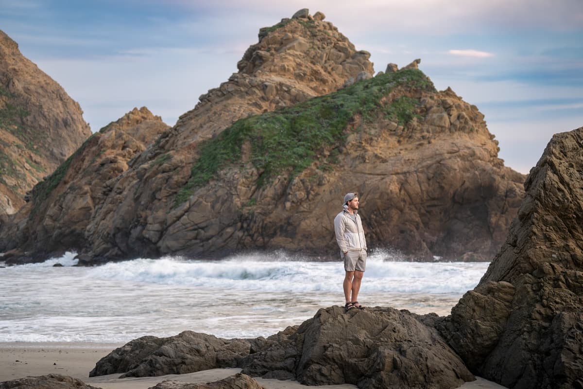 Man standing on a rock with a sea stack in the background along Pfeiffer Beach in Big Sur, California
