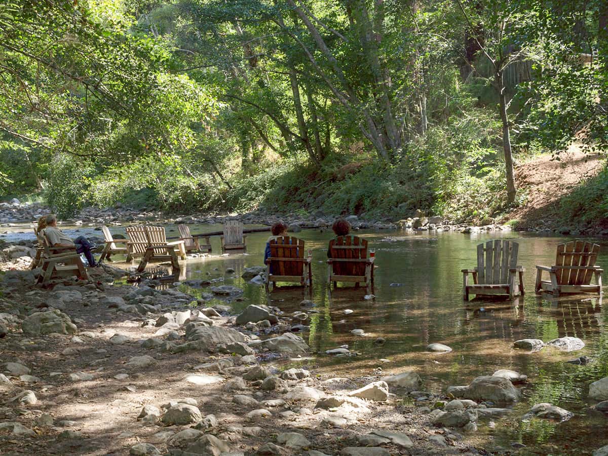 People sitting in Adirondack chairs in the Big Sur River at the bar for the Big Sur River Inn in Big Sur, California