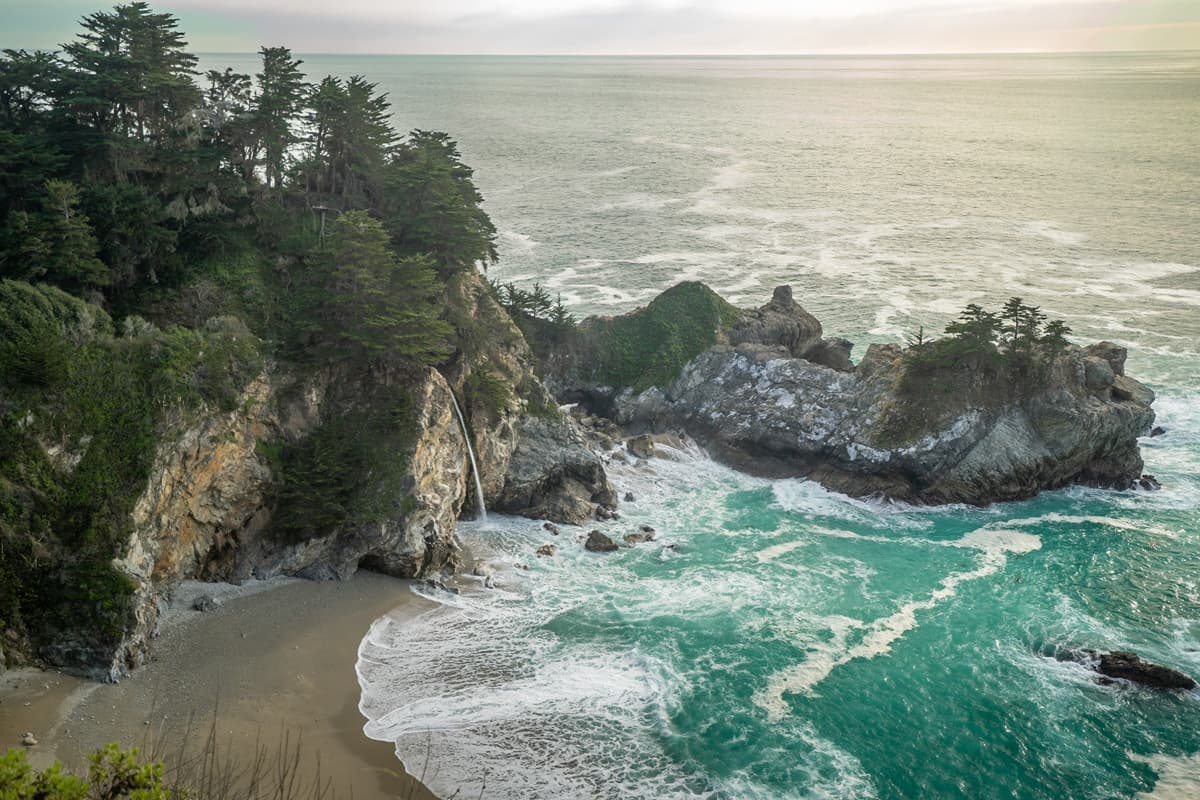 McWay Falls cascading from a rocky cliffside with pine trees on top in Julia Pfeiffer Burns State Park in Big Sur, California