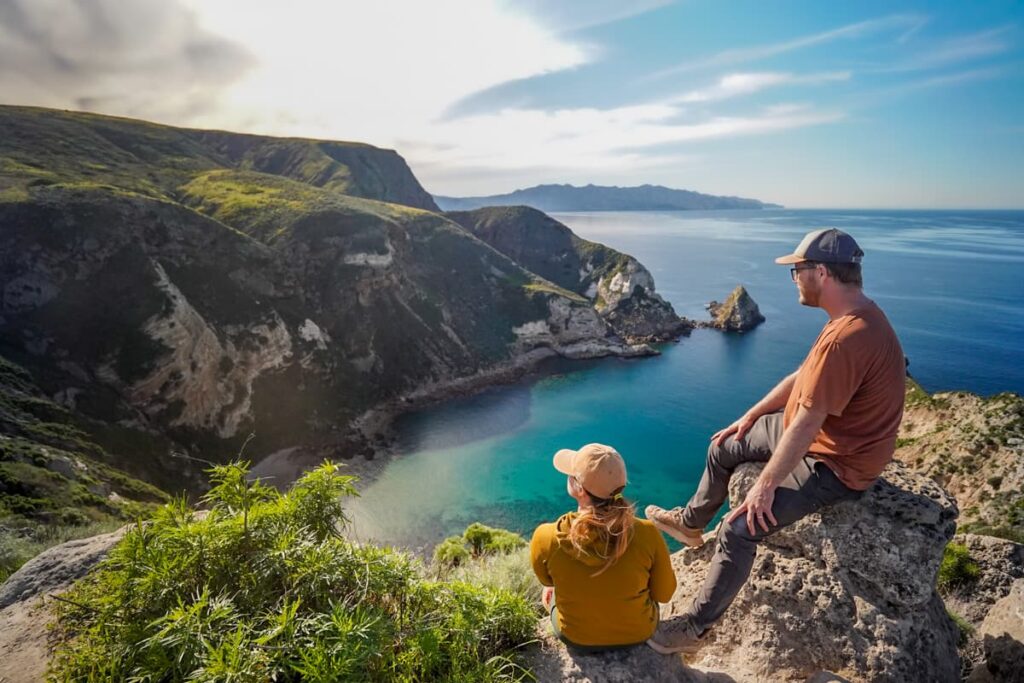 Couple sitting on a rocky outcropping overlooking Potato Harbor on Santa Cruz island on the Channel Islands National Park in California