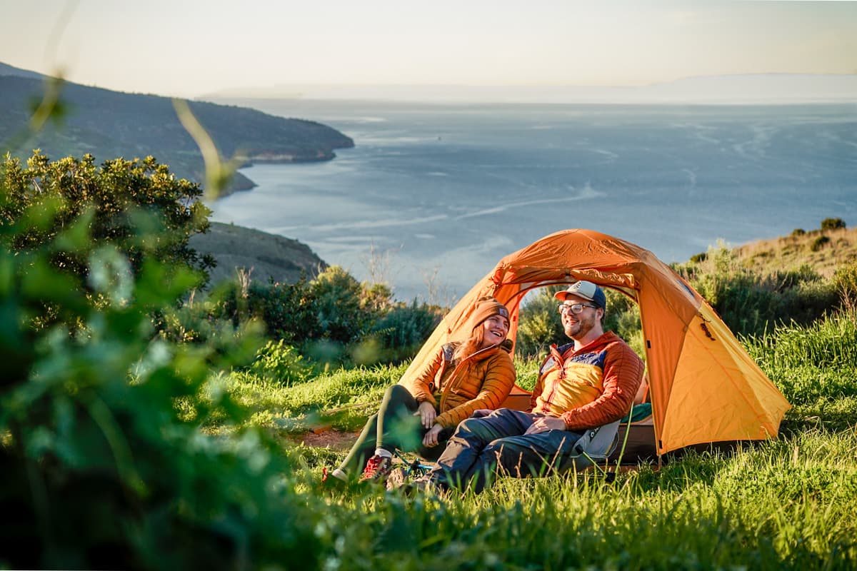 Smiling couple sitting in front of a tent at the Del Norte Campground on Santa Cruz island in Channel Islands National Park in California