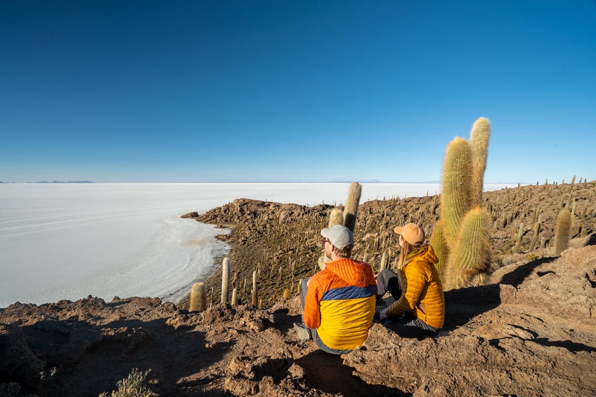 Couple sitting on a rocky outcropping near large cactuses on the Incahuasi Island in the Uyuni Salt Flats of Bolivia
