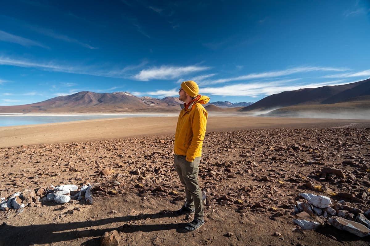 Man standing on a rocky shore of Laguna Verde with mountains in the background in the Altiplano of Bolivia