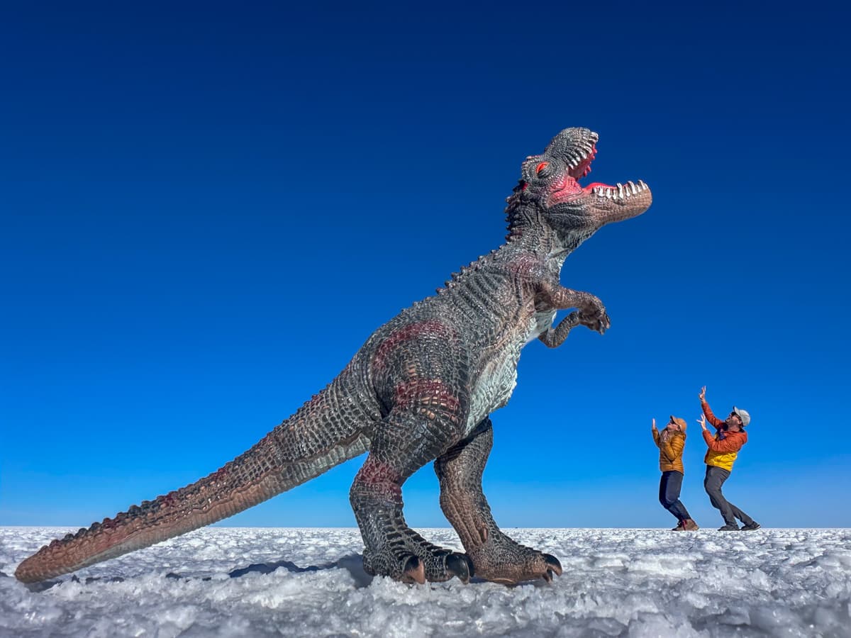 Couple posing with a dinosaur figurine on the Uyuni Salt Flats of Bolivia