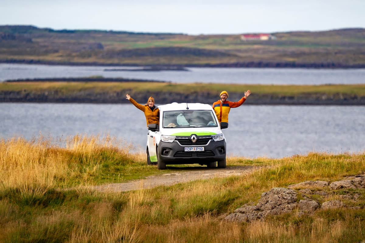 Couple sitting in their Happy 1 campervan model with a fjord in the background in Iceland