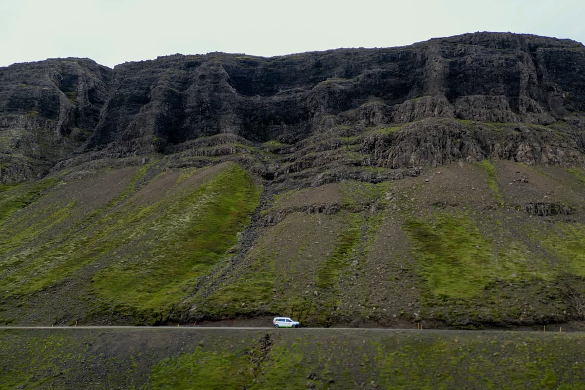 Campervan  driving down a road with mossy green cliffs in the background in Iceland