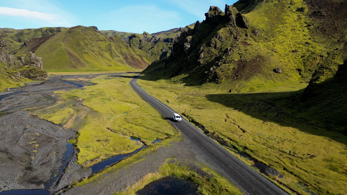 Campervan driving down the road surrounded by green rugged mountains by the Pakgil Campground in Iceland
