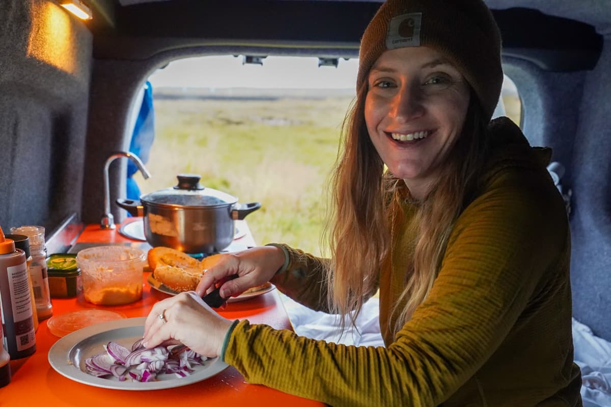 Smiling woman cutting onions while sitting on a bed in a campervan in Iceland