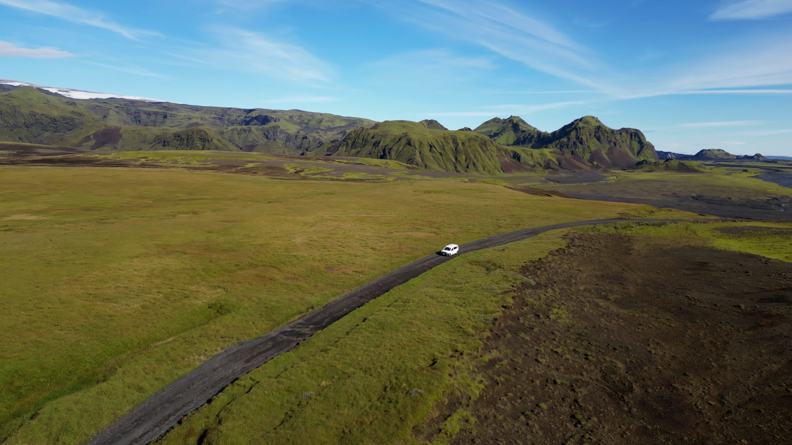Campervan driving down a gravel road with green mountains in the background near Pakgil in Iceland