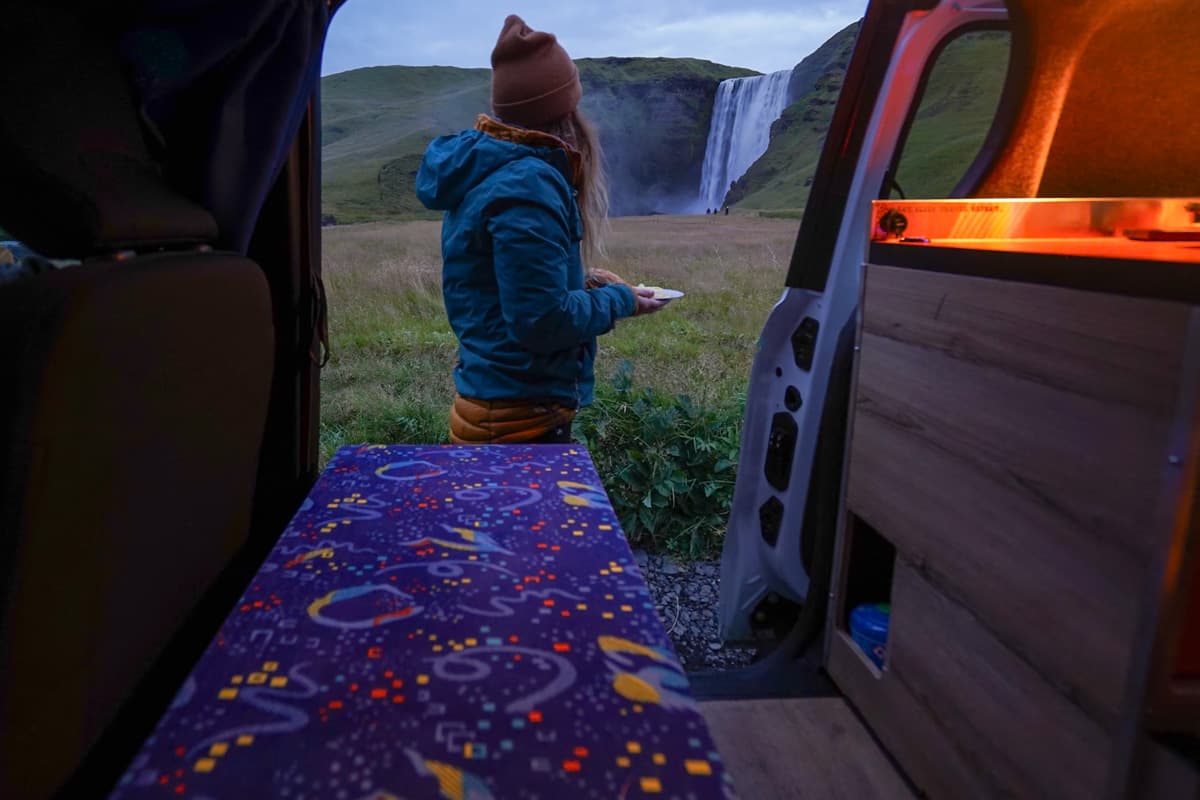 Woman holding a plate while standing outside of a campervan door with Selfoss in the background in Iceland