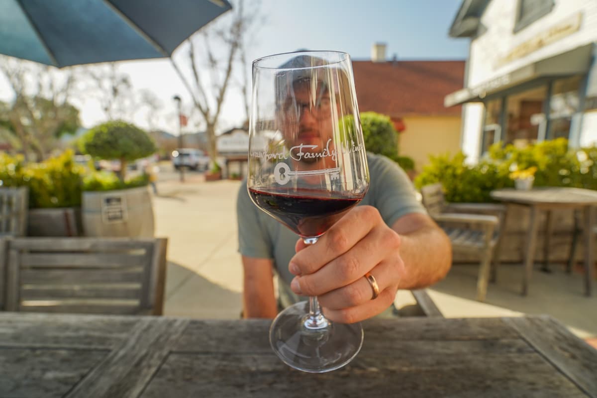 Man holding a glass of wine, sitting at a table at a tasting room, in Solvang, California
