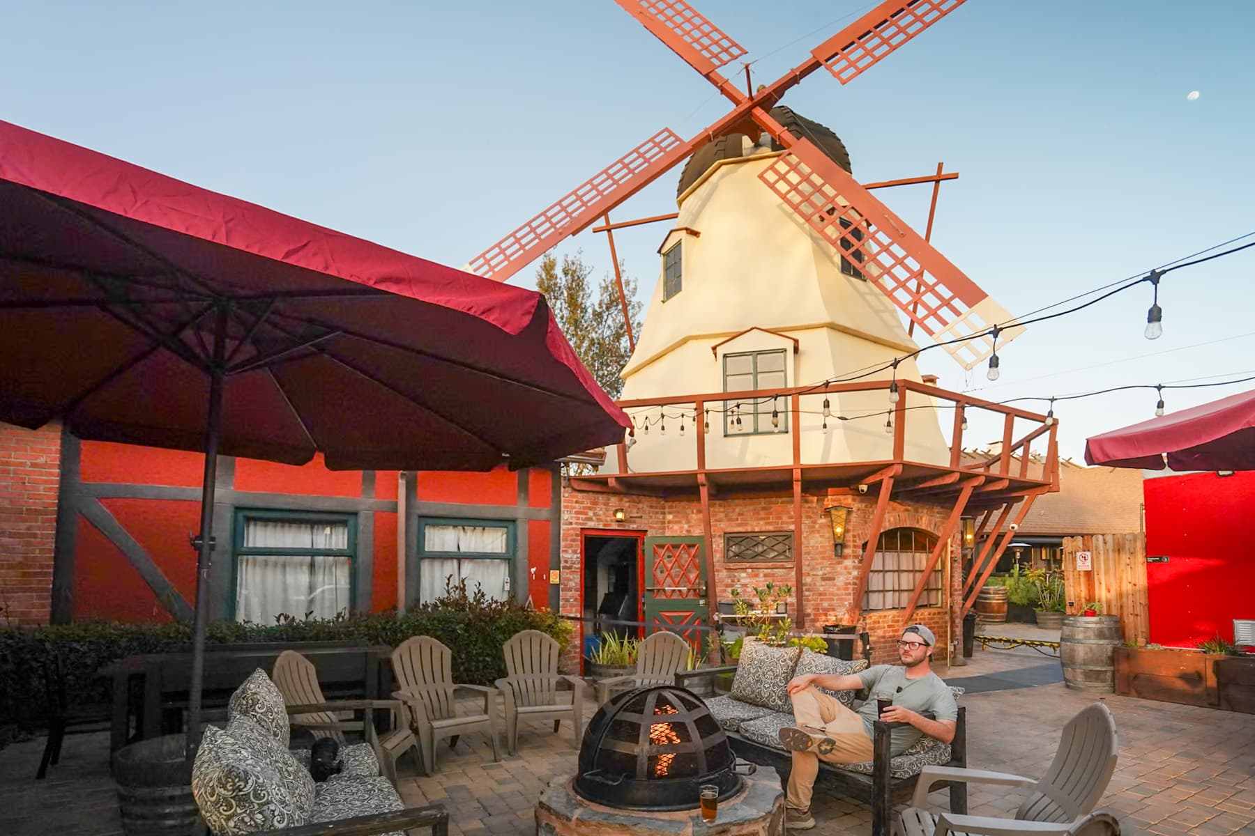 Man sitting around a campfire pit at the Solvang Brewery with a windmill in the background in Solvang, California
