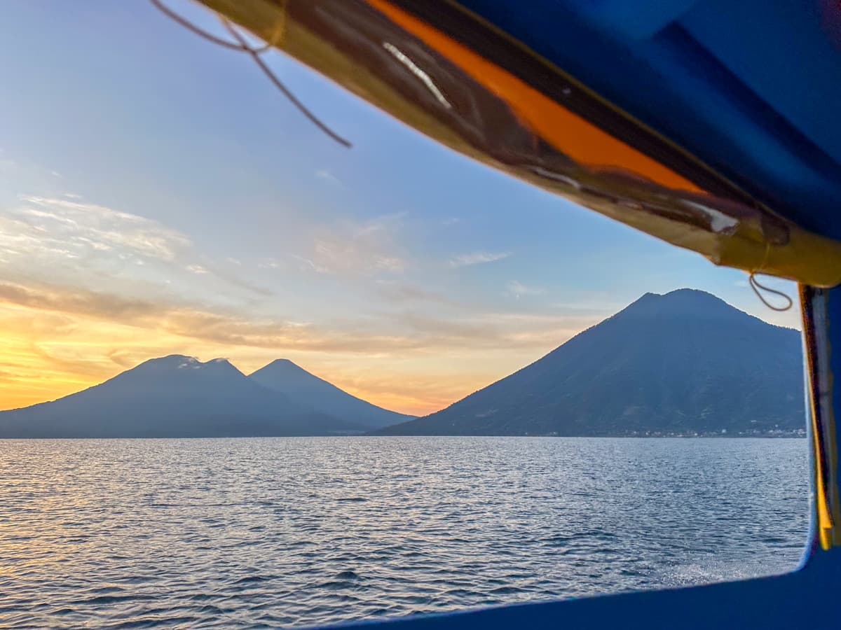 View out of a window of a lancha with volcanoes surrounding Lake Atitlan, Guatemala at sunrise