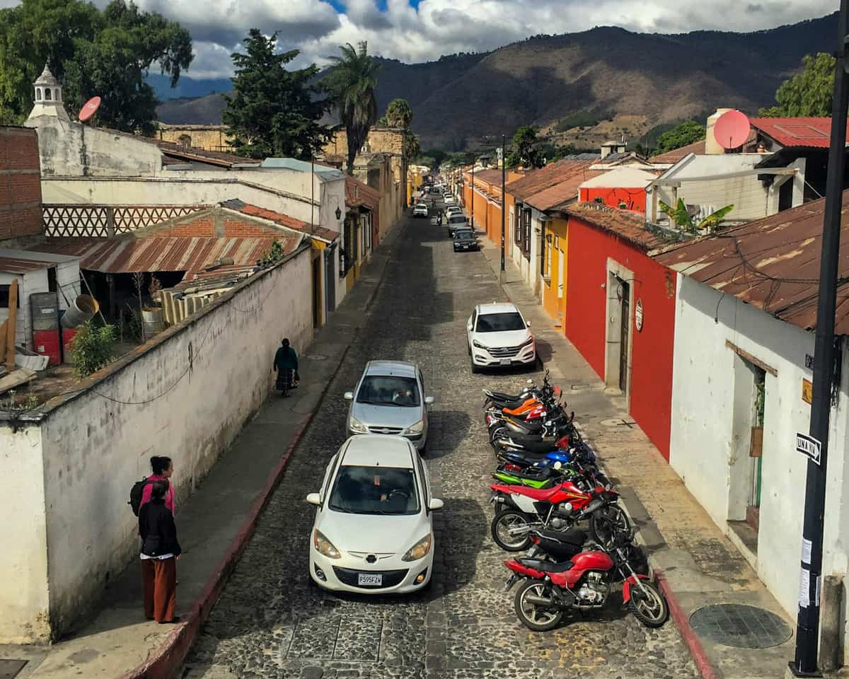 Car driving down a cobblestone street with colorful buildings lining the street in Antigua, Guatemala
