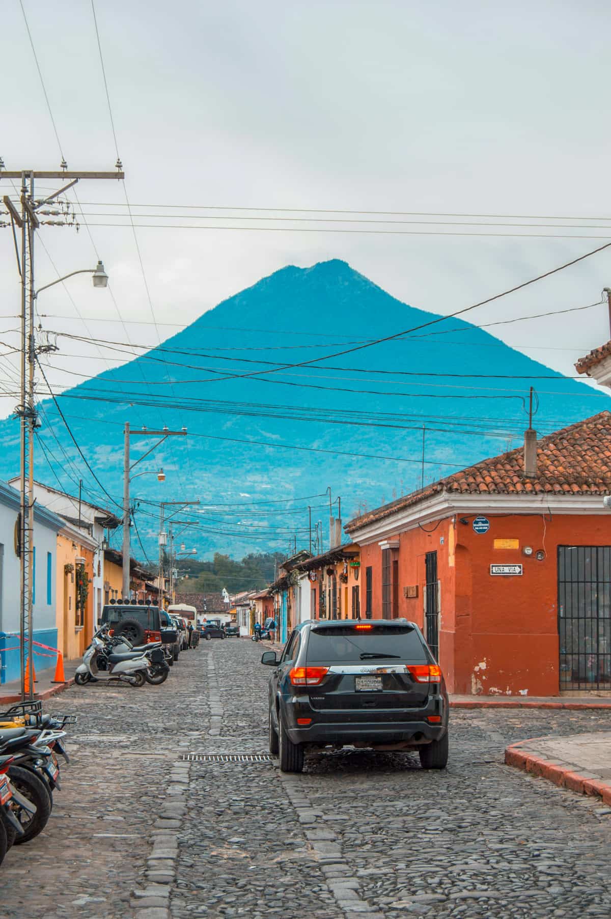 SUV driving down cobblestone street with colorful buildings and volcanoes in the background in Antigua, Guatemala
