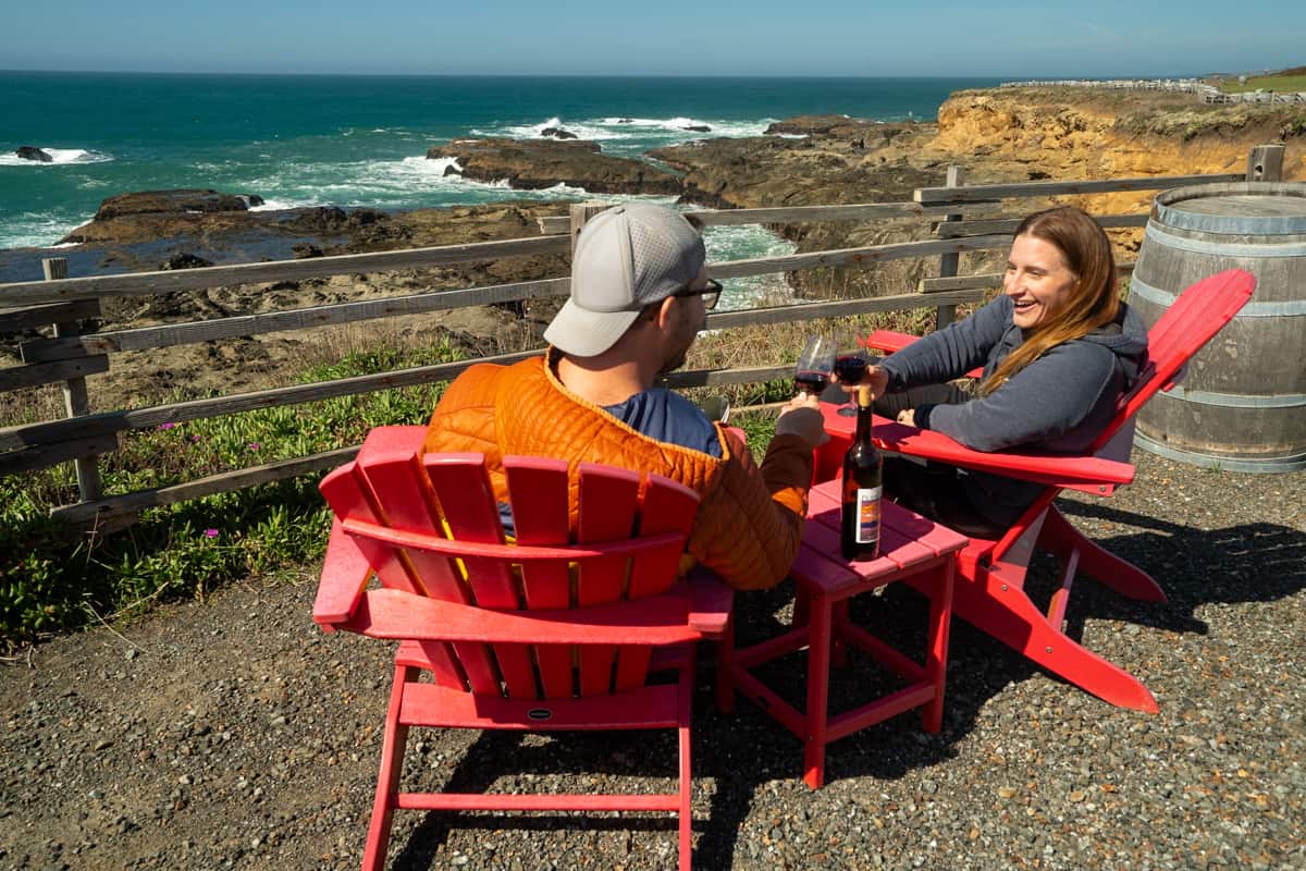 Couple cheersing a glass of wine while sitting in Adirondack chairs at Pacific Star Winery in Fort Bragg, California 