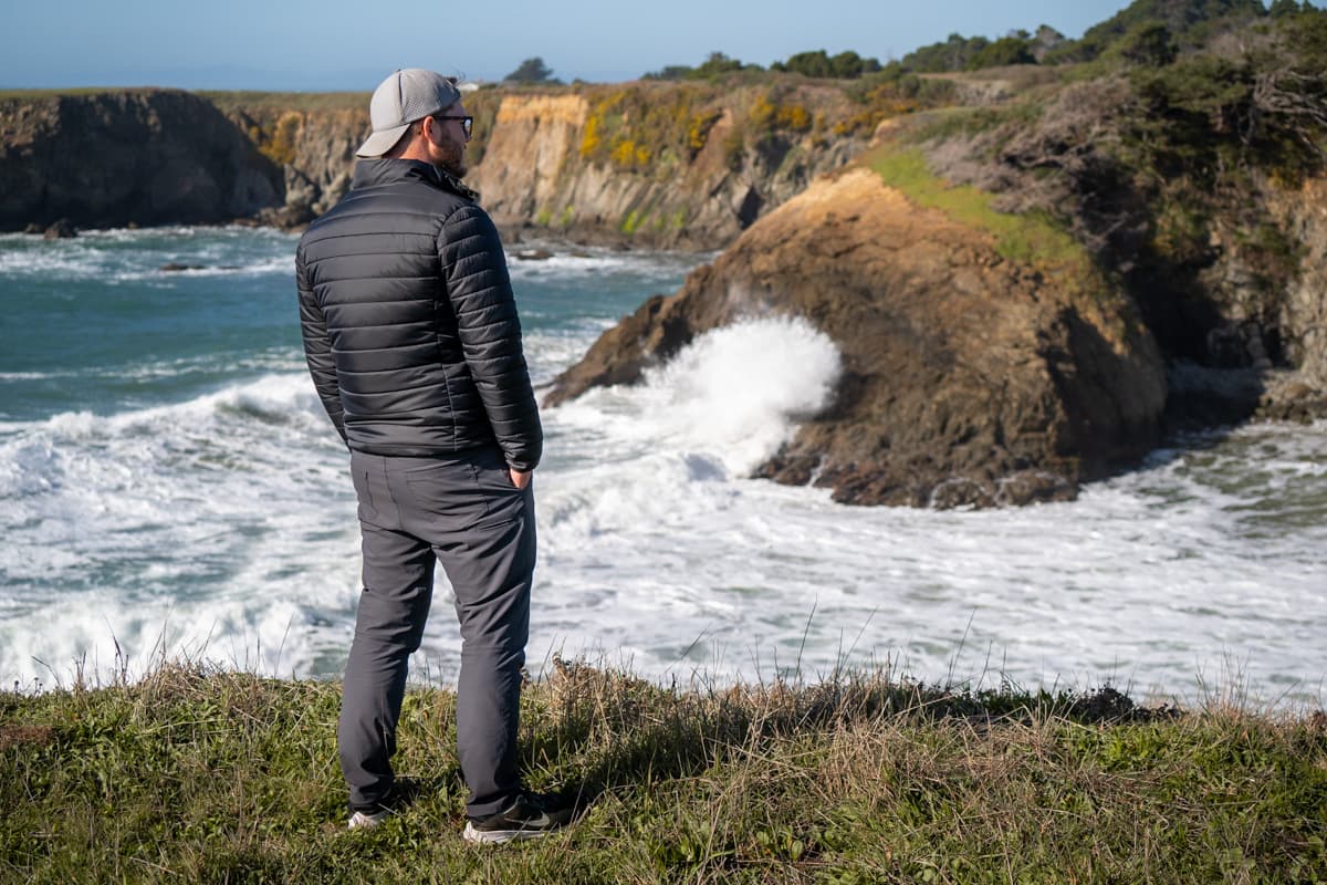 Man standing on a headland overlooking a wave crashing against a rugged cliffside in Jug Handle State Nature Preserve in Mendocino, California