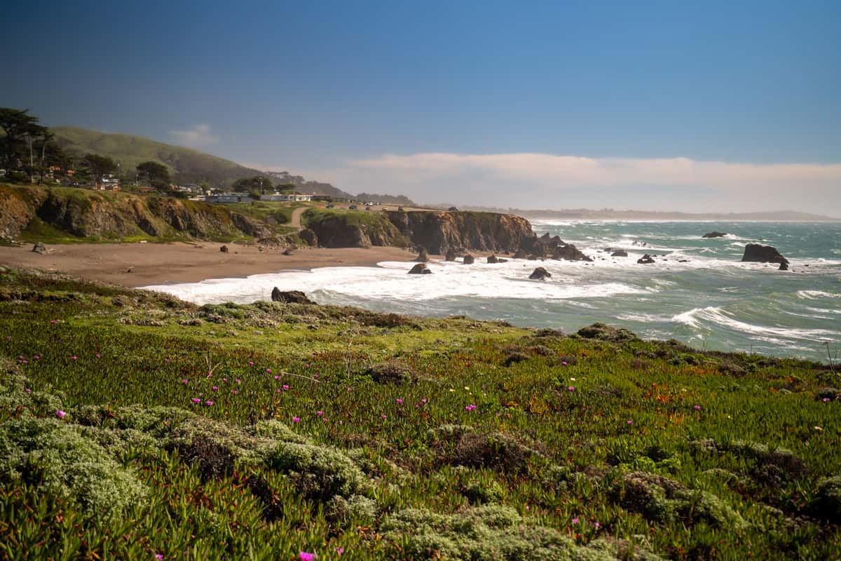 Buildings perched on windswept bluffs over a sandy beach with sea stacks in Navarro Point Preserve in Albion, California