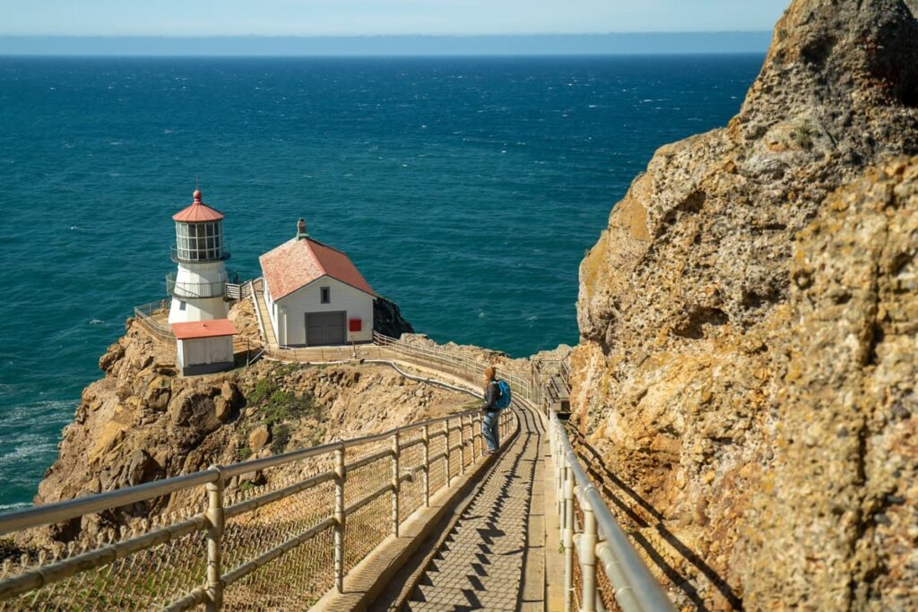 Woman standing on the stairs leading to the Point Reyes Lighthouse with the Pacific Ocean in the background in Point Reyes National Seashore in California