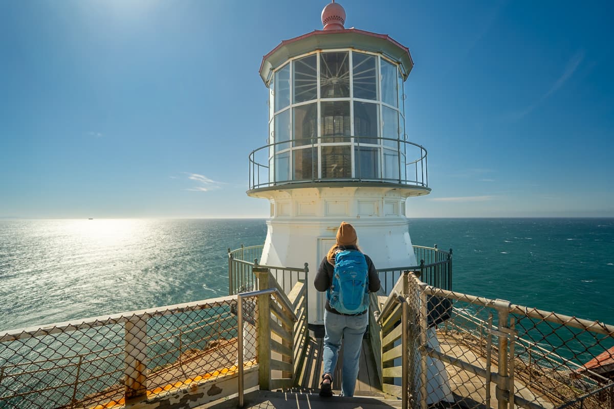 Woman walking down the stairs towards Point Reyes Lighthouse with the Pacific Ocean in the background in Point Reyes National Seashore in California