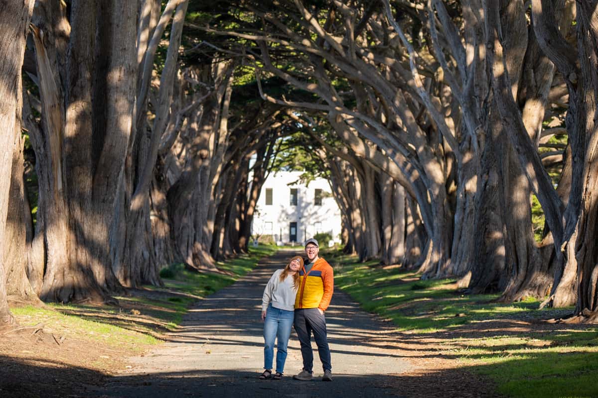 Smiling couple standing under the cypress tree tunnel in Point Reyes National Seashore in California