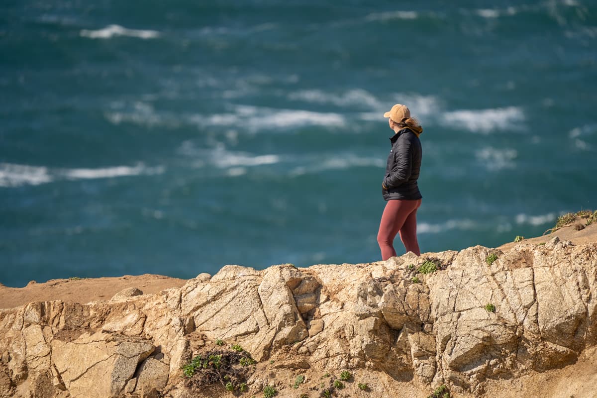 Woman standing on top of a rugged cliff by Tomales Point on the Tomales Point Trail in Point Reyes National Seashore in California